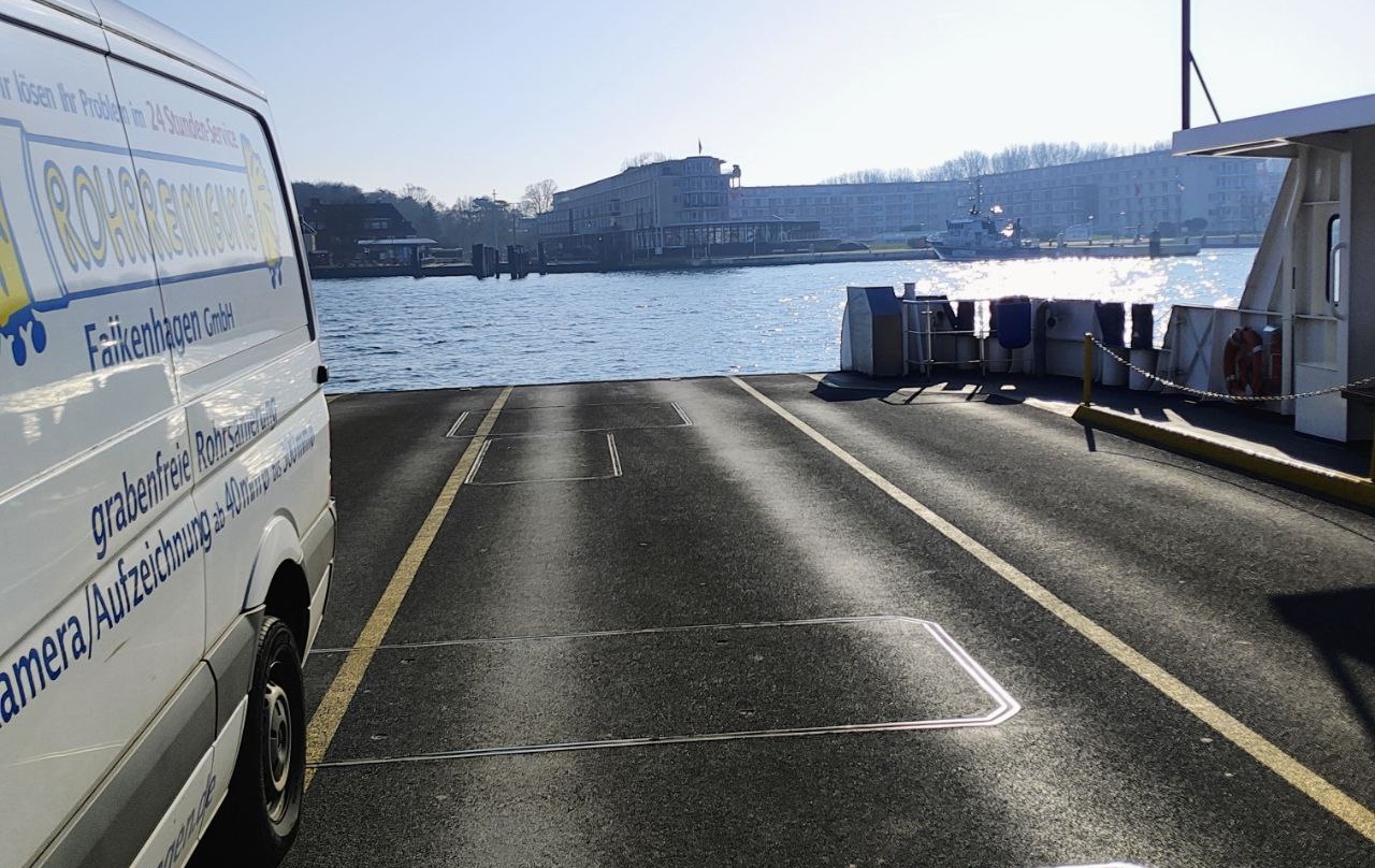 Einsatzfahrzeug der Rohrreinigung Falkenhagen GmbH auf einer Fähre über die Trave in Lübeck, weißer Transporter mit Firmenbeschriftung für grabenfreie Rohrsanierung und Kamerabefahrung